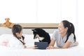 Young mother and small daughter playing with Maltese dog on bed. Happy mother holding her child using tablet with dog on bedroom Royalty Free Stock Photo