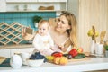 Young mother smiling, cooking and playing with her baby daughter in a modern kitchen. Healthy food concept. Working at home. Woman Royalty Free Stock Photo