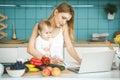 Young mother smiling, cooking and playing with her baby daughter in a modern kitchen. Using phone. Healthy food concept. Working Royalty Free Stock Photo
