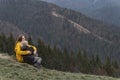 Young mother with son sit on hillside. Mother and son rest and sit in an embrace on mountains background