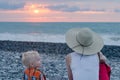 Young mother and son sitting on beach against sea and sunset. Single mother concept