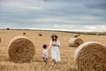 Young mother and son walking near stacks of straw - stacked bales of hay left after harvesting, farm field with Royalty Free Stock Photo