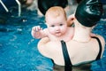 Young mother, swimming instructor and happy little girl in paddling pool. Teaches infant child to swim. Enjoy. Mom holds Royalty Free Stock Photo