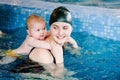 Young mother, swimming instructor and happy little girl in paddling pool. Teaches infant child to swim. Enjoy. Mom holds hand Royalty Free Stock Photo