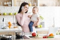 Young mother talking on phone, holding her baby at kitchen Royalty Free Stock Photo