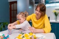 Young mother teaching and little daughter are painting Easter eggs sitting at the kitchen. Concept of preschool Royalty Free Stock Photo