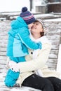 Young mother with toddler boy sitting on bench in winter park. Woman playing and hugging with cute baby son. Royalty Free Stock Photo