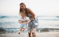 Young mother with a toddler boy standing on beach on summer holiday, having fun. Royalty Free Stock Photo