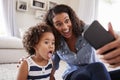 Young mother and toddler daughter taking selfie at home