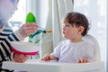 Mother try to feeding a toddler boy with a spoon in a chair Royalty Free Stock Photo