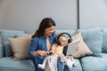 Young mother trying to entertain her newborn baby by playing cartoons and funny videos on digital tablet while sitting on sofa at