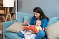 Young mother trying to entertain her newborn baby by reading a fairytale books while sitting on sofa at home. Woman read a book Royalty Free Stock Photo