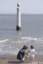 a young mother and a two year old girl contemplate at a seagull perched on a column on a pier above the Tagus estuary in Lisbon,