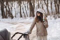 Young mother walking with baby in stroller and drinking hot coffee in winter park Royalty Free Stock Photo