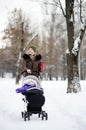 Young mother walking with baby in stroller in winter park Royalty Free Stock Photo