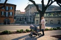 Young mother walking with her baby in stroller in the city on sunny winter day. Elegant pretty woman pushing baby pram Royalty Free Stock Photo