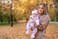 Young mother walking with her newborn daughter in the autumn park. Mother holding the girl in her arms, smiling and Royalty Free Stock Photo