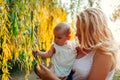 Young mother walking in summer park with her baby. Curious infant touching tree leaves