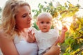 Young mother walking in summer park with her baby. Curious infant touching tree leaves