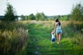 Young mother walks with her little daughter barefoot on a country road at sunset, view from the back. The nanny walks