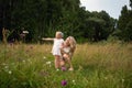 A young mother walks through a meadow with a little girl. Summer day, wildflowers, birch