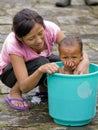 Young mother is washing her daughter in a small bucket