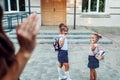 Young mother waving to her daughters before classes outdoors primary school seeing them off. Family saying goodbye Royalty Free Stock Photo