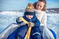 A young mother, woman with child, boy, son of 3 years old, in the winter outside in warm clothes, sitting on a tubing Royalty Free Stock Photo