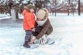 Young mother woman straightens children`s skis, little boy son 3 years. Winter forest park, background snow drifts