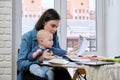 Young mother work with baby in her arms at home office