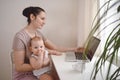 Young mother work studying from home with laptop computer during quarantine, little cute toddler baby on lap. Home office,