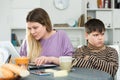 Young mother working at laptop and unhappy preteen son