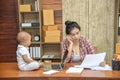 Young mother workingn on the phone with her daughter sitting on desk.  Beautiful busy working mother. Single mother concept Royalty Free Stock Photo