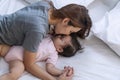 Motherhood kissing her lovely daughter while baby girl sleeping calm on the white bed. Newborn toddler girl with her mom