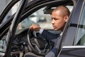 Young businessman sitting in car door opened holding steering wheel looking aside thoughtful close-up