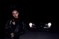 A young  mulatto girl in a leather jacket and black clothes poses on an abandoned sand road. at night in the light of car Royalty Free Stock Photo