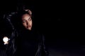 A young mulatto girl in a leather jacket and black clothes poses on an abandoned sand road. at night in the light of car Royalty Free Stock Photo