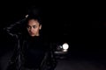 A young mulatto girl in a leather jacket and black clothes poses on an abandoned sand road. at night in the light of car Royalty Free Stock Photo