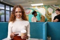 Young multi-ethnic woman texts with cellphone, standing in busy open plan office Royalty Free Stock Photo