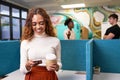 Young multi-ethnic woman texts with cellphone, standing in busy open plan office Royalty Free Stock Photo