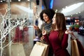 Young multiethnic diverse race women with paper shopping bags near decorated shopwindow. Girl pointing by finger at