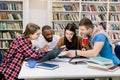 Young multiethnical college students at the library studying together, they are smiling, looking at book while finding Royalty Free Stock Photo