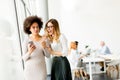 Young multiracial businesswomen smiling, while other businesspeople working in background