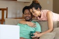 Young multiracial couple embracing while watching laptop together in living room at home Royalty Free Stock Photo