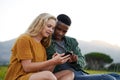 Young multiracial couple sitting and looking down while using mobile phone in field Royalty Free Stock Photo