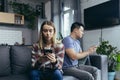 Young multiracial family, quarreling sitting on the couch in the room, man and woman on the phone, turned in different directions