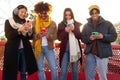 Young multiracial happy smiling people standing in a row looking at mobile phones during sunny winter day. Royalty Free Stock Photo