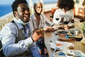 Young multiracial people eating and drinking red wine while wearing protective masks - Social distance concept - Focus on african Royalty Free Stock Photo