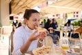 Young multiracial woman has lunch in an Italian restaurant on the summer terrace, biting a slice of delicious pizza Royalty Free Stock Photo