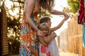 Young mum holding her blonde daughter girls on her arms smiling. Warm sunset light. Family summer travel vacations at